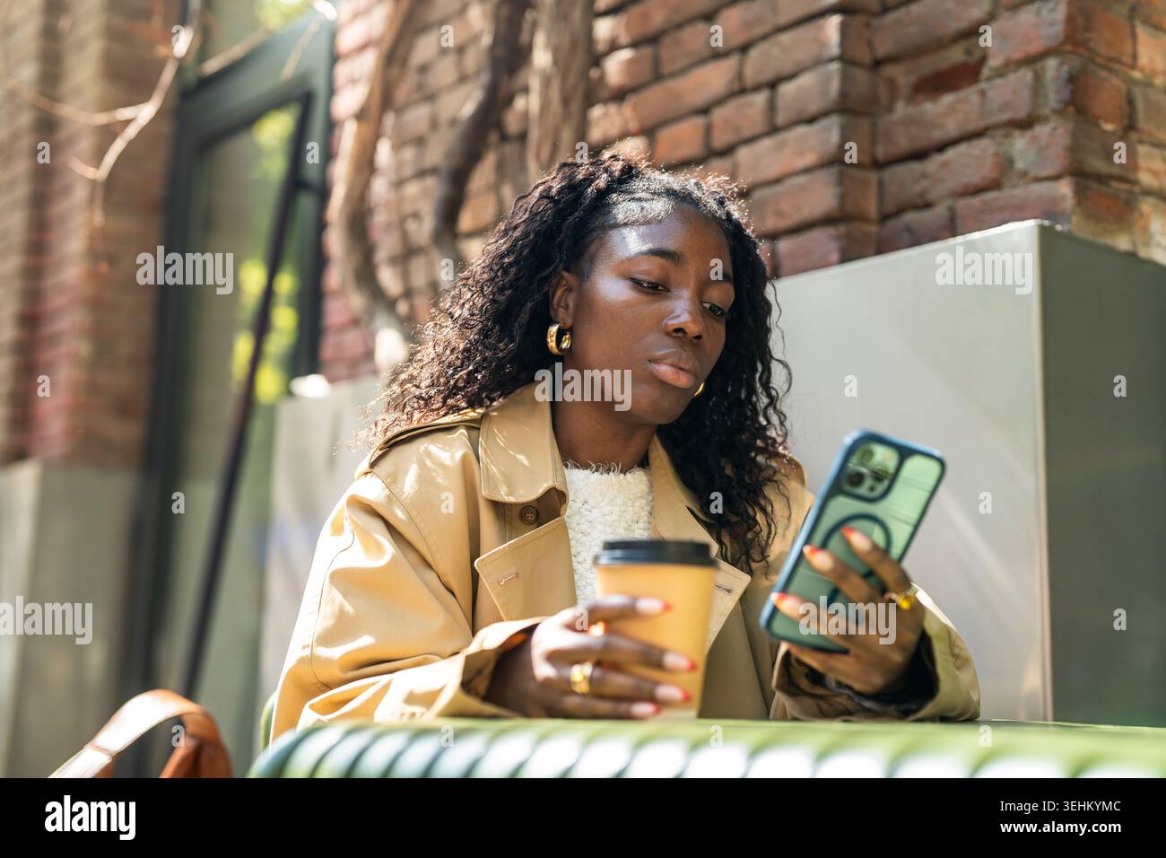 Pensiva donna afro-americana che scorre i media online sullo smartphone mentre riposa in un bar all'aperto. Foto Stock