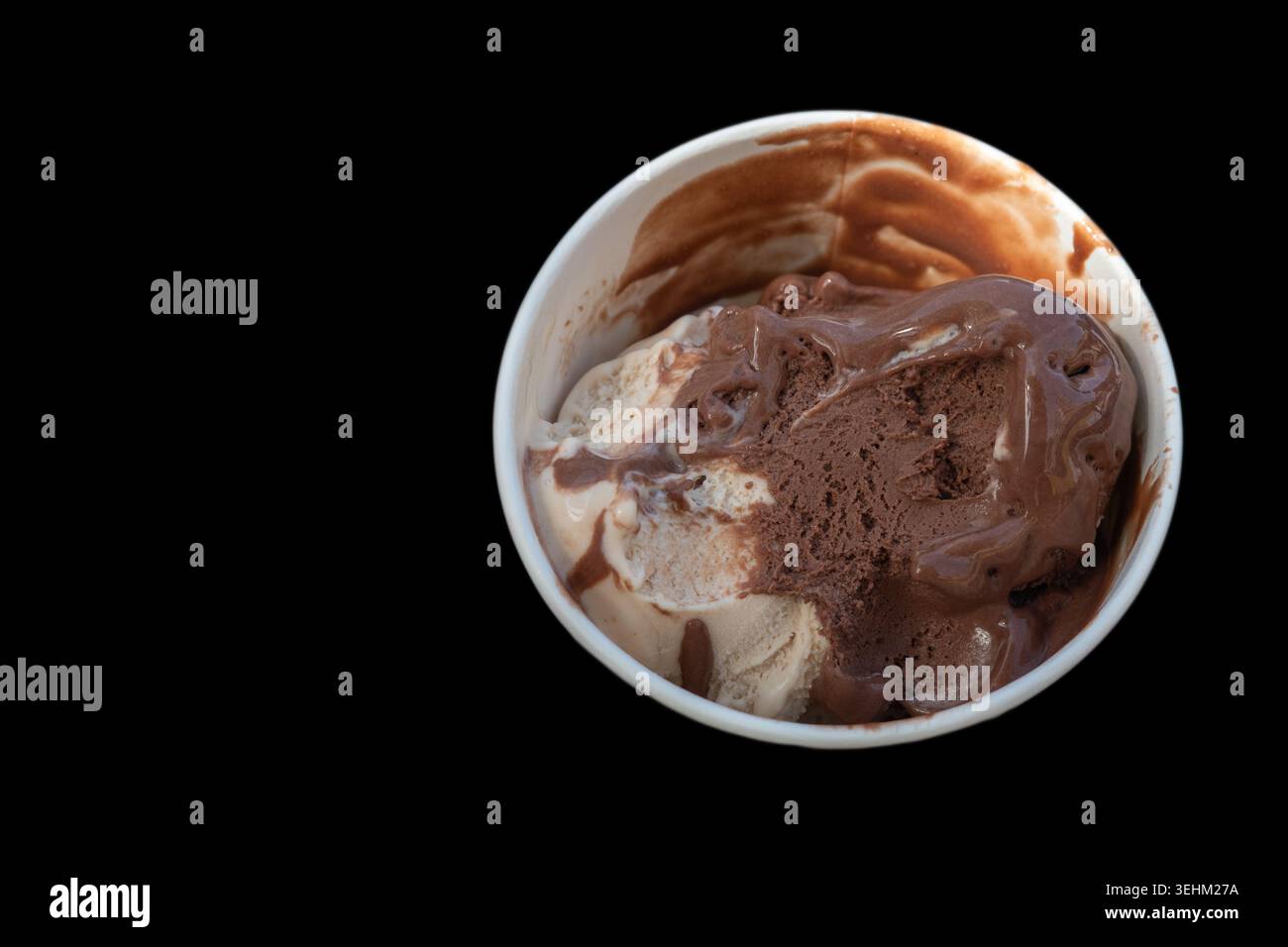 Una tazza piena di cioccolato e gelato alla vaniglia si trova su uno sfondo nero. I vortici di salsa al cioccolato si mescolano con il gelato, mostrando sapori ricchi. Foto Stock