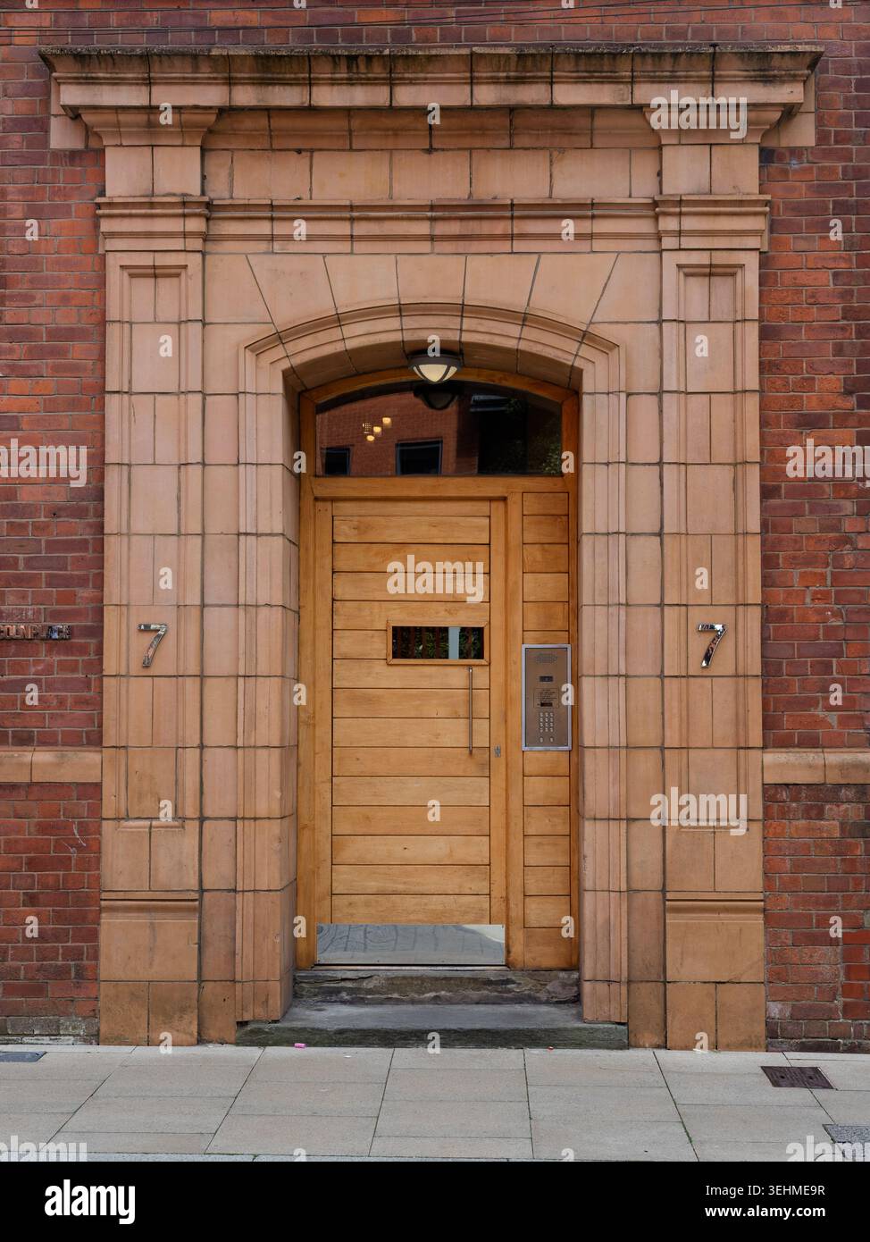Porta vittoriana ad arco in pietra arenaria con una porta in legno e un pannello intercom contemporanei, 7 Hulme Street, Oxford Road Corridor, Manchester. Foto Stock