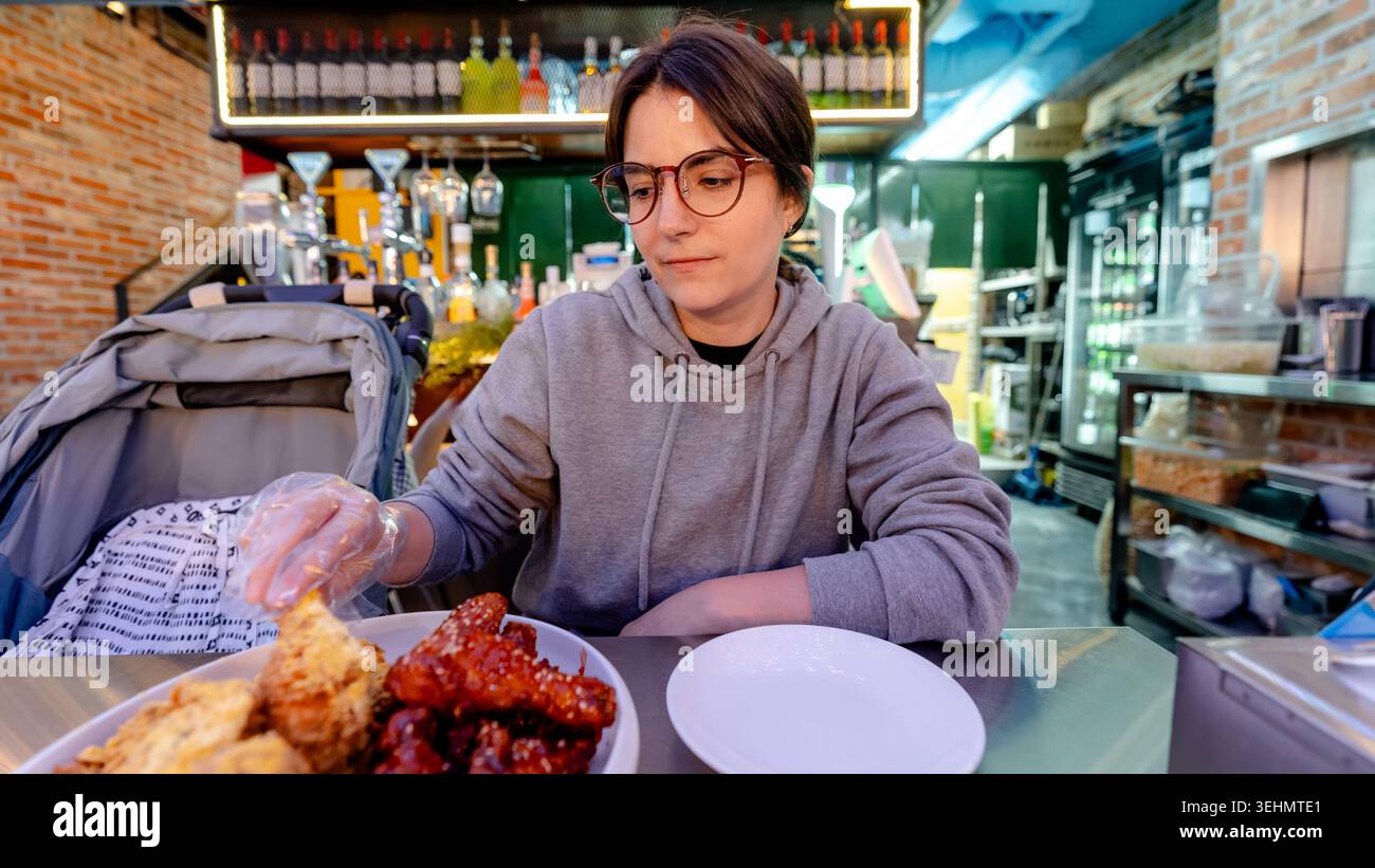 Viaggiatore che assaggia pollo yangnyeom piccante e dolce con burro croccante in un ristorante informale a Seoul, Corea del Sud, con piatti sul tavolo e un caldo bancone da bar Foto Stock