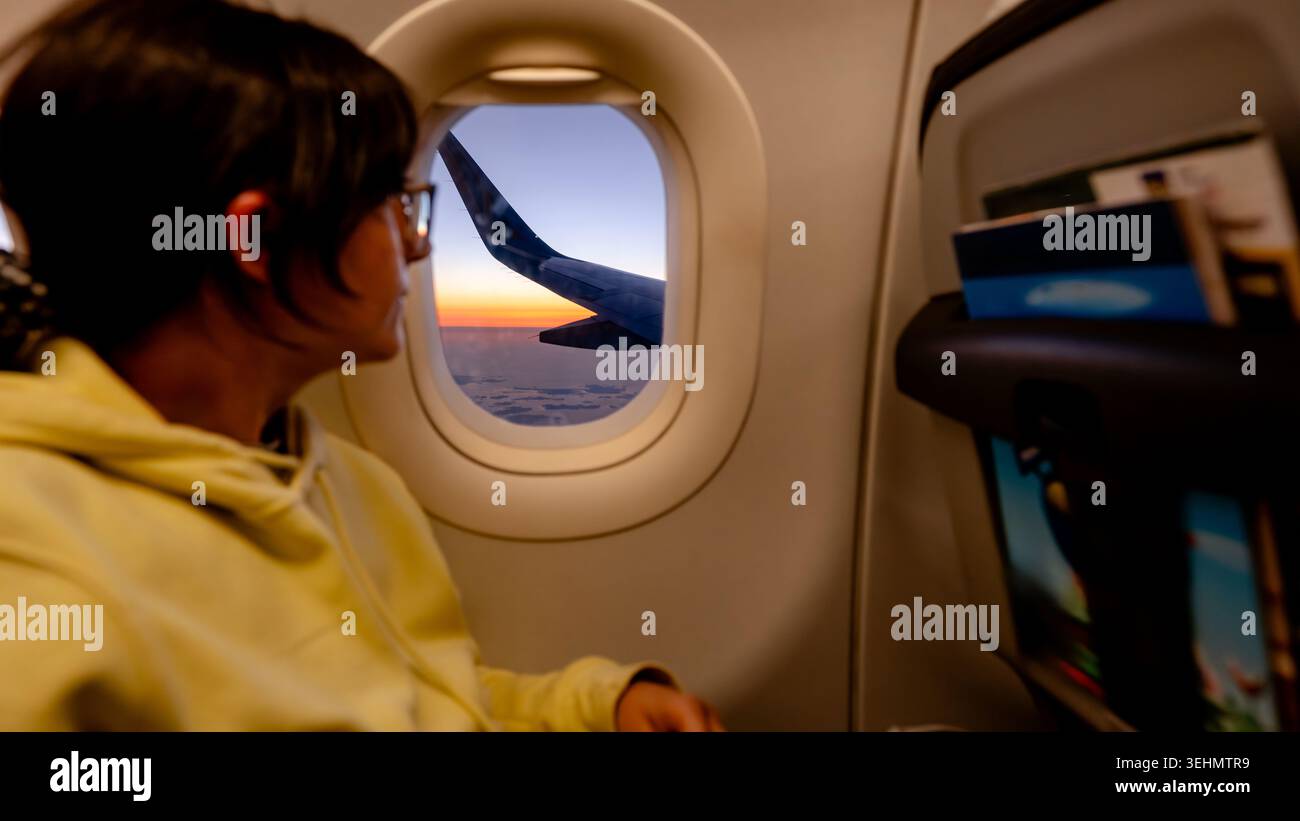 Il viaggiatore si siede accanto alla finestra di un aereo, guardando un tramonto vibrante sopra le nuvole e la silhouette delle ali, catturando momenti tranquilli di viaggio aereo, avventura, Foto Stock