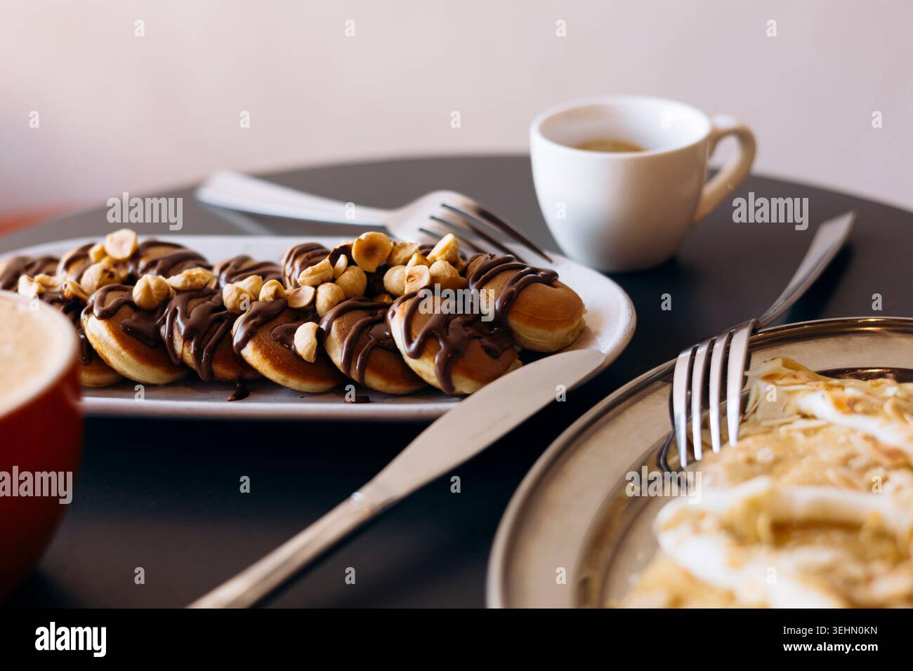 Tavolo della colazione con mini pancake conditi con cioccolato e ricoperti di nocciole, più pancake con mela e formaggio spalmabile, serviti con caffè fresco Foto Stock