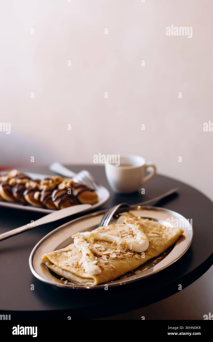 Colazione accogliente con mini pancake conditi con cioccolato e nocciole, più pancake di mele condite con formaggio spalmabile, serviti con una tazza di caffè Foto Stock