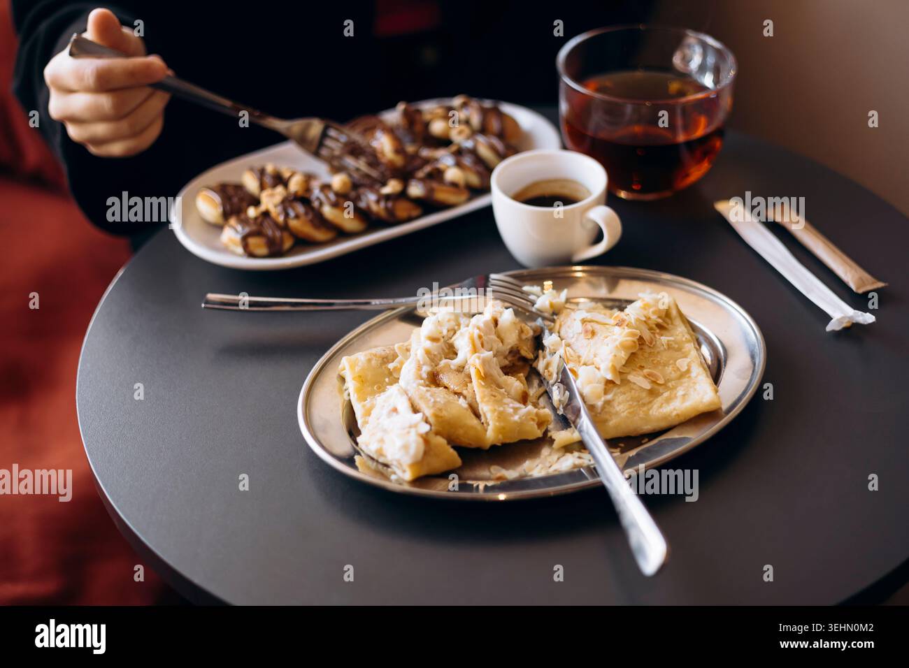 Colazione accogliente con mini pancake ricoperti di cioccolato e nocciole, più pancake ripieni di mela e formaggio spalmabile, serviti con caffè caldo Foto Stock