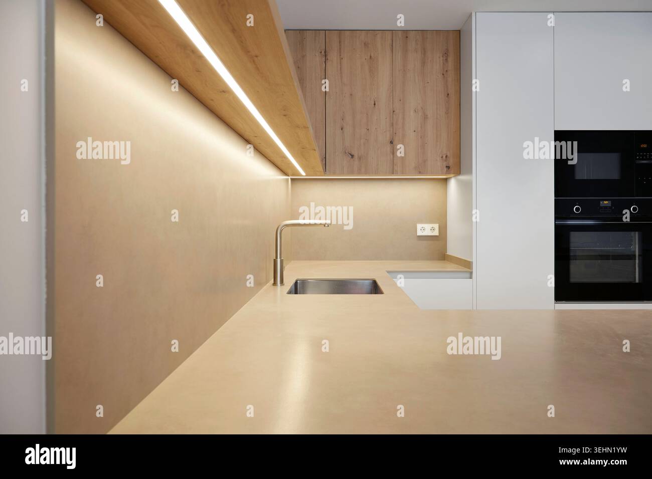 Interni luminosi e moderni in stile minimalista con mobili in legno, elettrodomestici integrati e luci a strisce LED soffuse sopra un piano di lavoro e un lavandino puliti, i Foto Stock