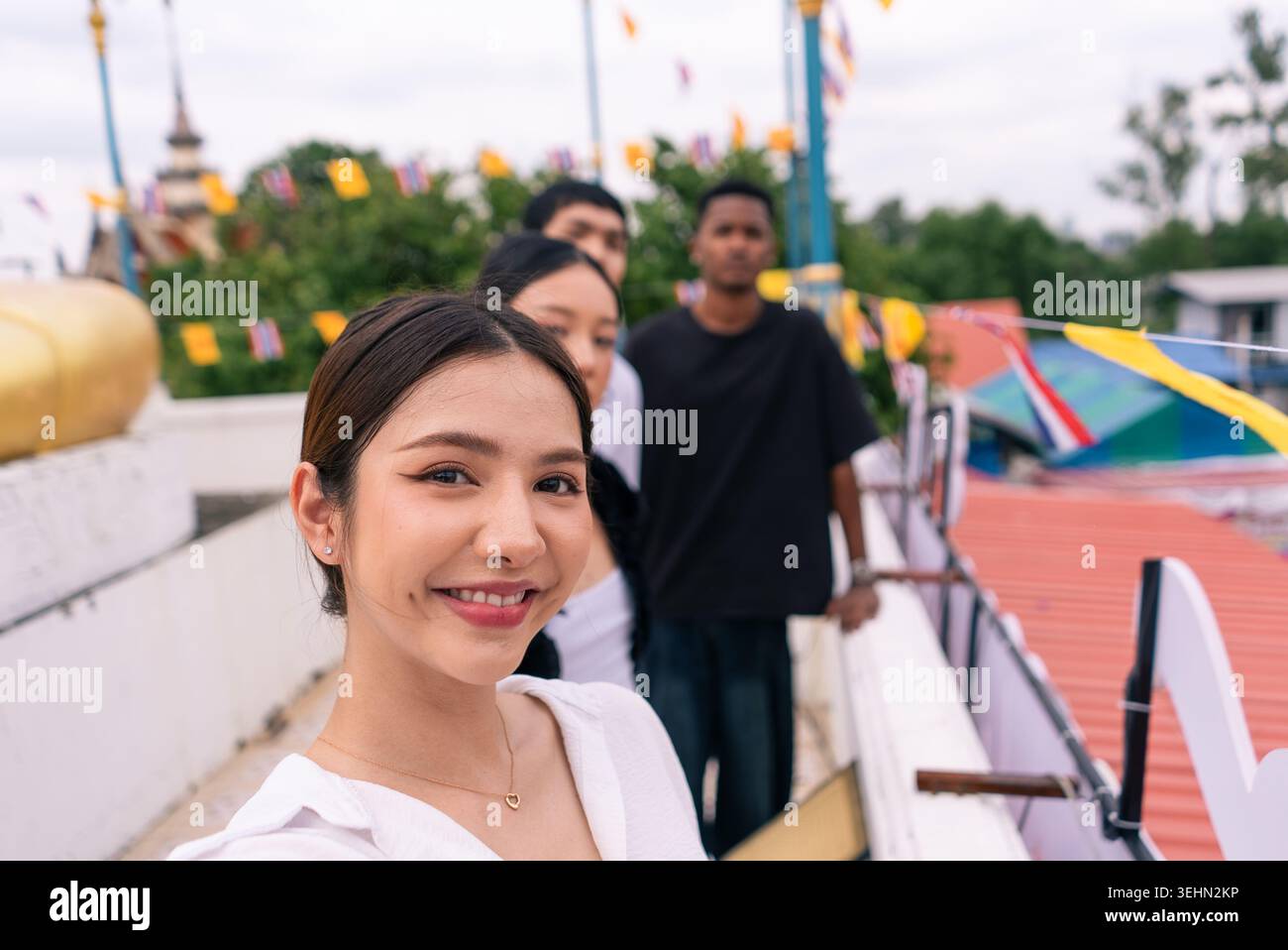 Giovane donna asiatica sorridente, scattando selfie con diversi amici sul tetto del tempio Foto Stock