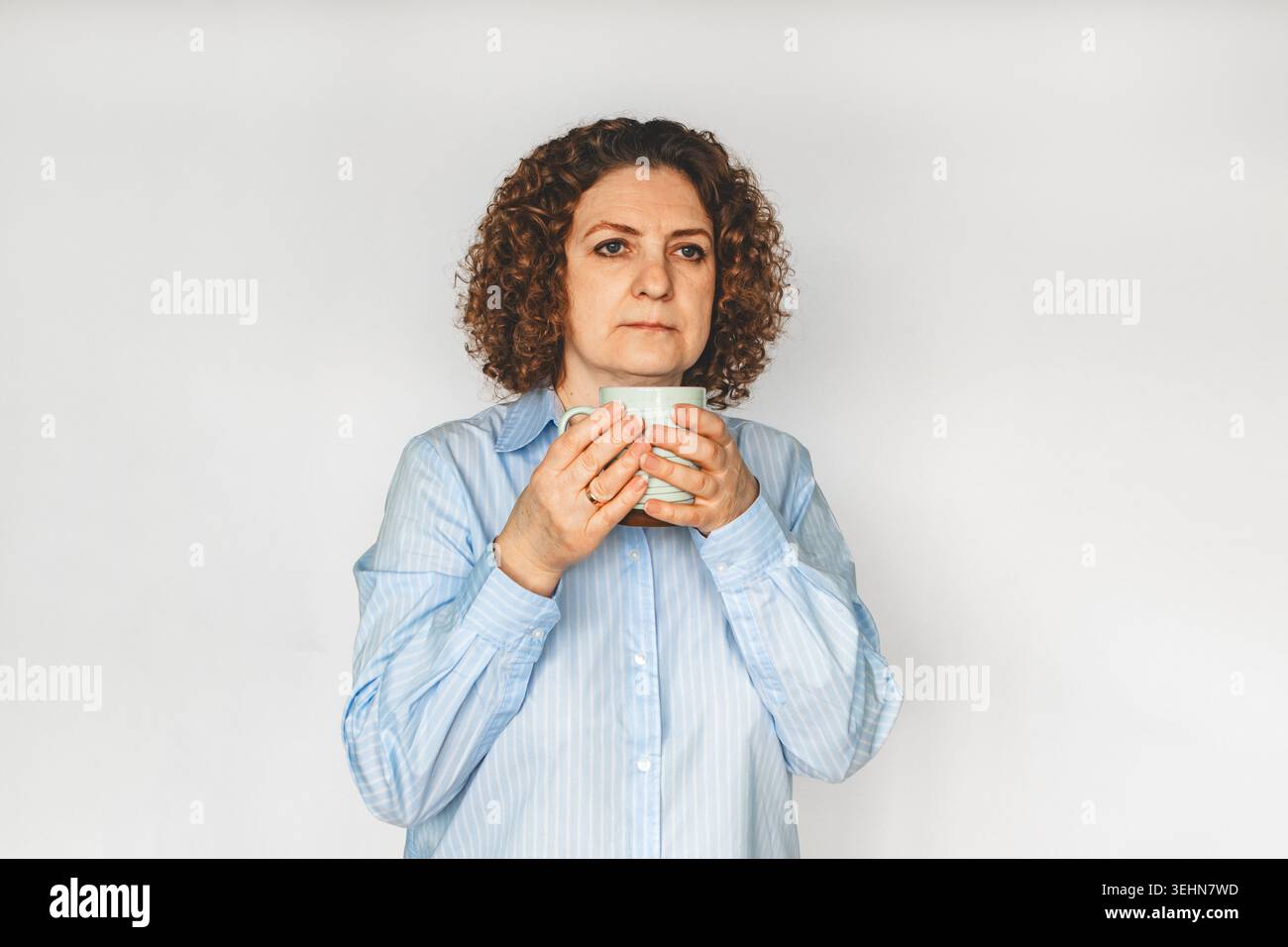 Donna di mezza età che tiene in mano una tazza da caffè, ritratto accurato in camicia blu su sfondo bianco Foto Stock