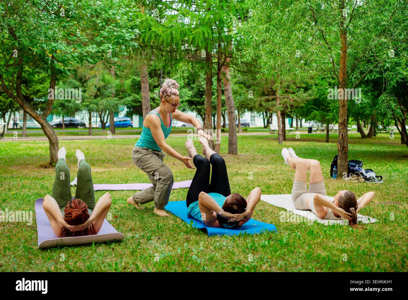Donne in abbigliamento sportivo beige e verde che tengono il ponte in posa su tappeti erbosi insieme nel parco cittadino. Bridge pose, abbigliamento sportivo, tappetini, insieme, parco, donne. Foto Stock