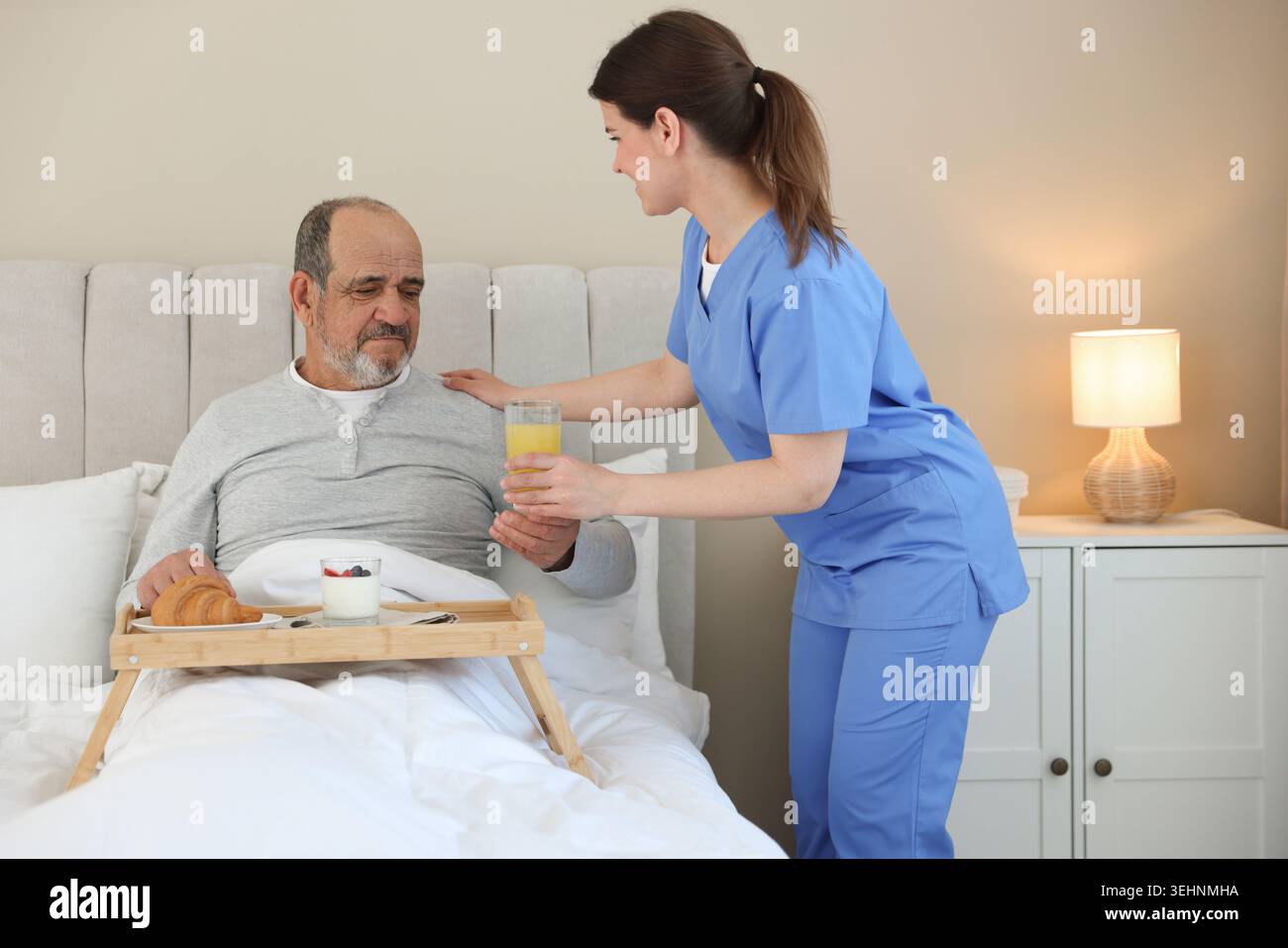 Assistente che fa colazione a un anziano a letto a casa Foto Stock