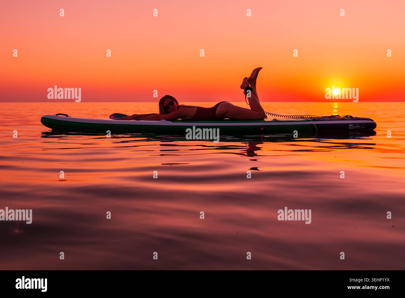 24 maggio 2026. Antalya, Turchia. Silhouette di donna che si rilassa a bordo di un paddle board sul mare calmo durante il tramonto arancione Foto Stock
