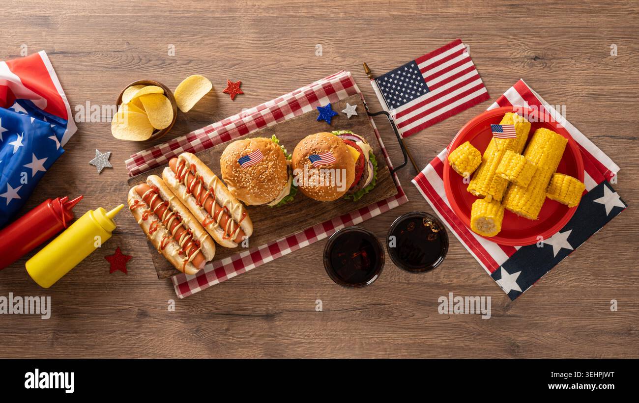 Vista dall'alto di hamburger hot dog, corn cola e decorazioni patriottiche su un tavolo di legno per la celebrazione dell'American Independence Day con spazio per fotocopie. Banner Foto Stock