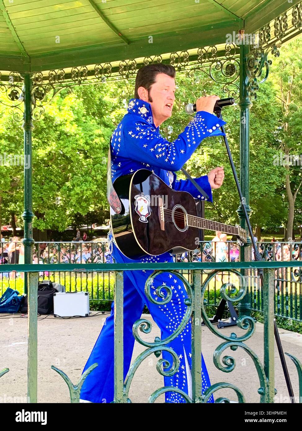 L'artista tributo a Elvis intrattiene la folla all'Abington Park Northampton, Inghilterra, cantando in estate con la folla che guarda vicino alla tribuna - Immagine stock catturata con smartphone