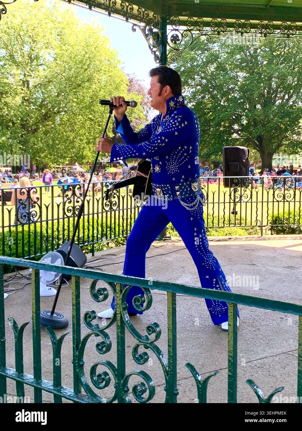 L'artista tributo a Elvis intrattiene la folla all'Abington Park Northampton, Inghilterra, cantando in estate con la folla che guarda vicino alla tribuna - Immagine stock catturata con smartphone