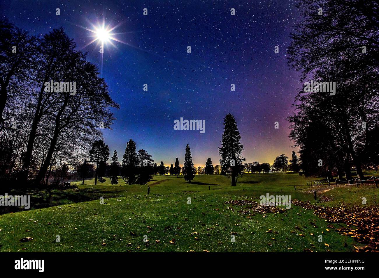 Campagna inglese illuminata dalla luna sotto un cielo pieno di stelle, con gli ultimi sussurri di tramonto che svaniscono nella notte surreale. Foto Stock