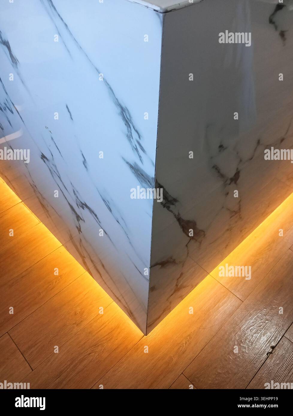 Moderno angolo bancone in marmo bianco con calda illuminazione LED sotto l'armadio su pavimento in legno Foto Stock