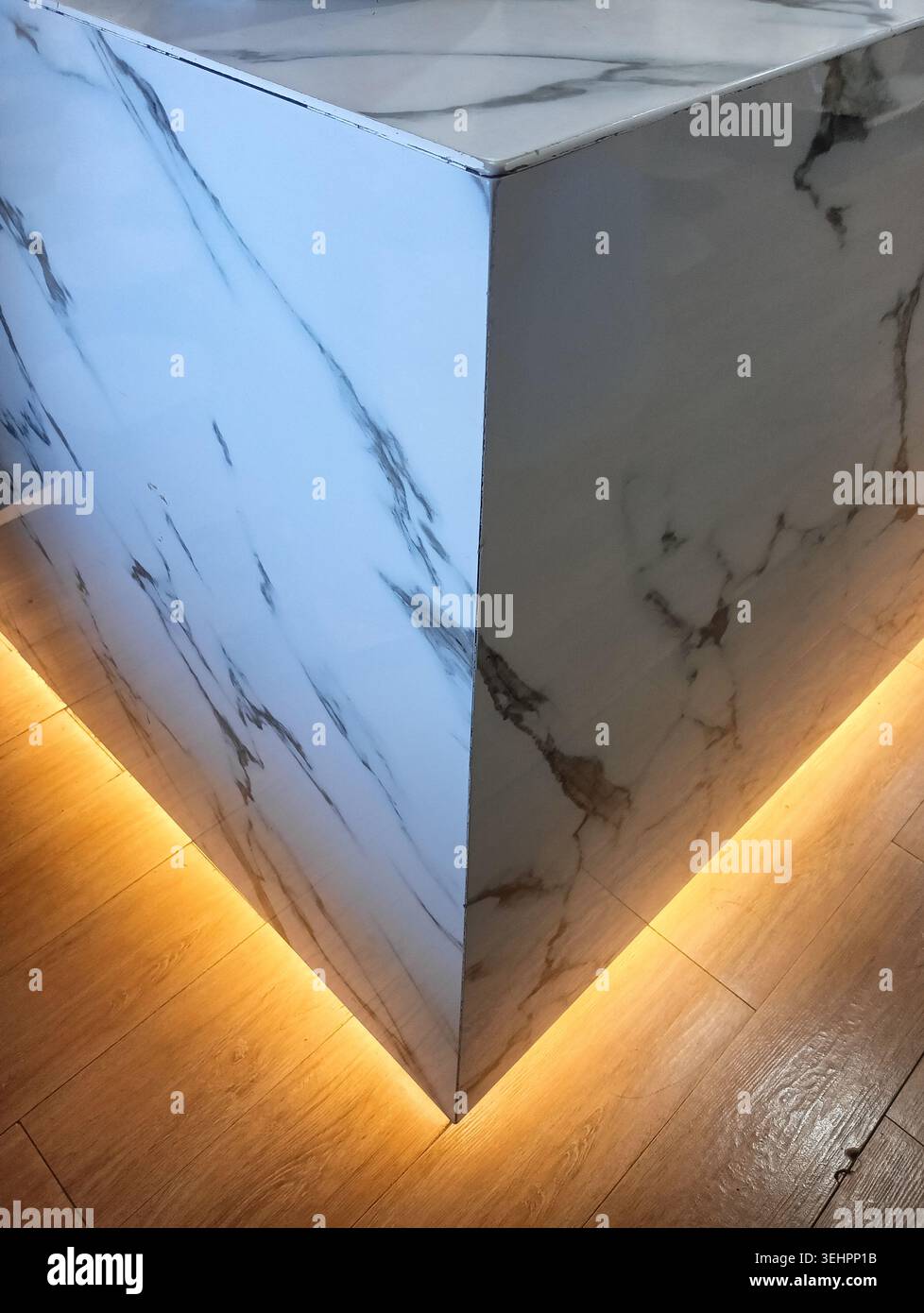 Moderno angolo bancone in marmo bianco con calda illuminazione LED sotto l'armadio su pavimento in legno Foto Stock