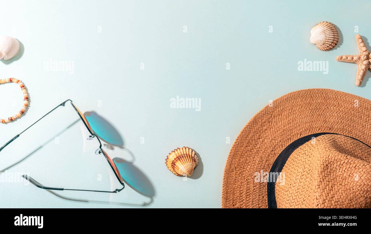 Accessori da spiaggia estivi con cappello di paglia, occhiali da sole, conchiglie e stelle marine disposti su sfondo blu pastello. Vacanza tropicale e concetto di viaggio. Foto Stock