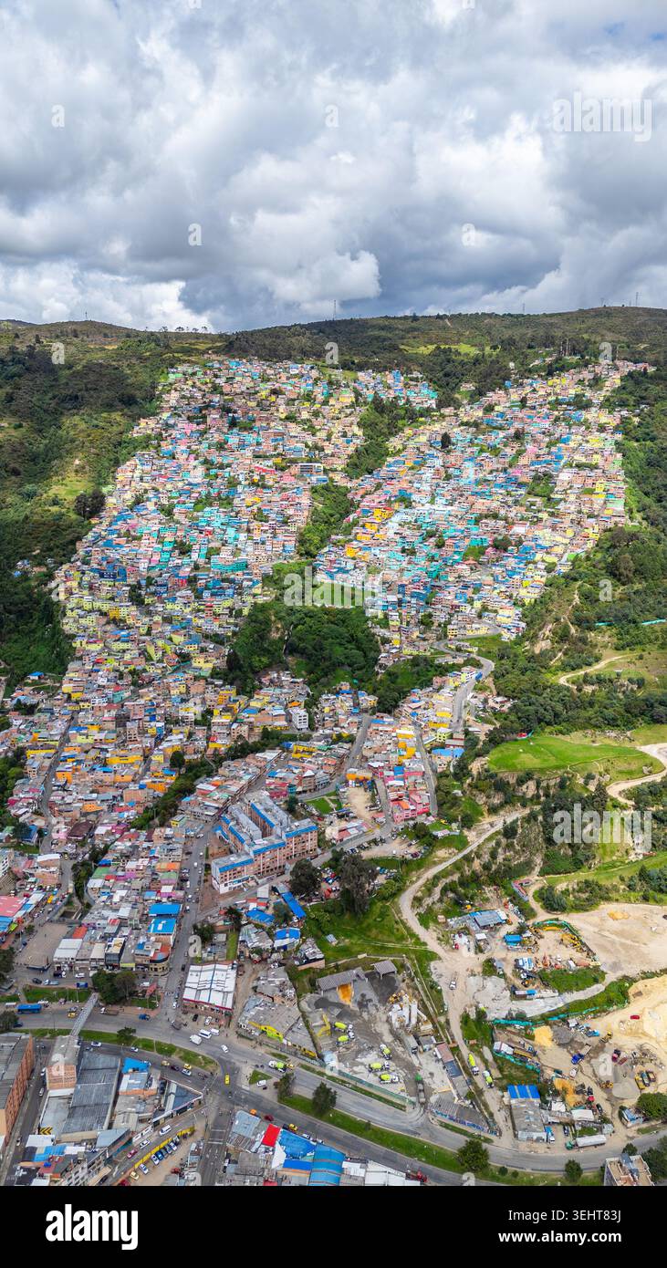 Case colorate su una collina a Bogotá, che mostrano la trasformazione urbana con macchie di verde e tetti colorati sotto un cielo nuvoloso. Foto Stock