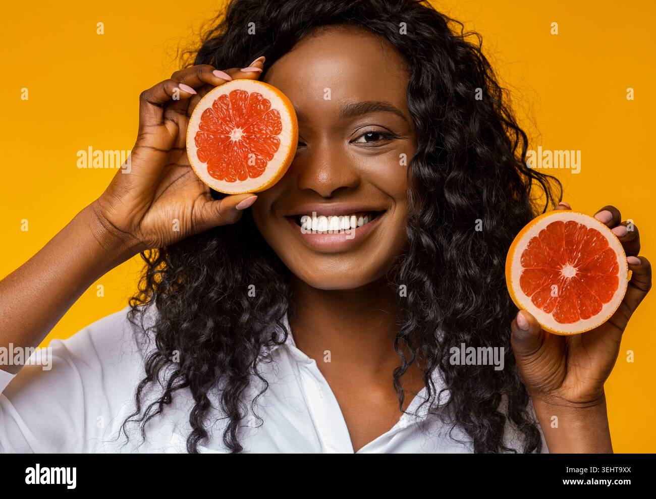 Donna sorridente mentre tiene in mano metà pompelmo su un vivace sfondo giallo Foto Stock