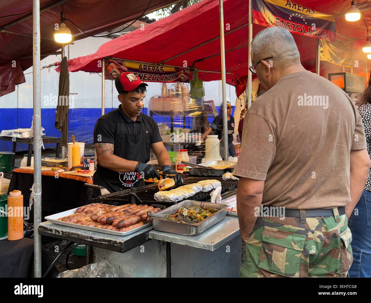 Un venditore prepara le arepas venezuelane in un affollato stand di Street food a Mercado de Antojitos, Coyoacán, città del Messico, Messico - Immagine stock catturata con smartphone