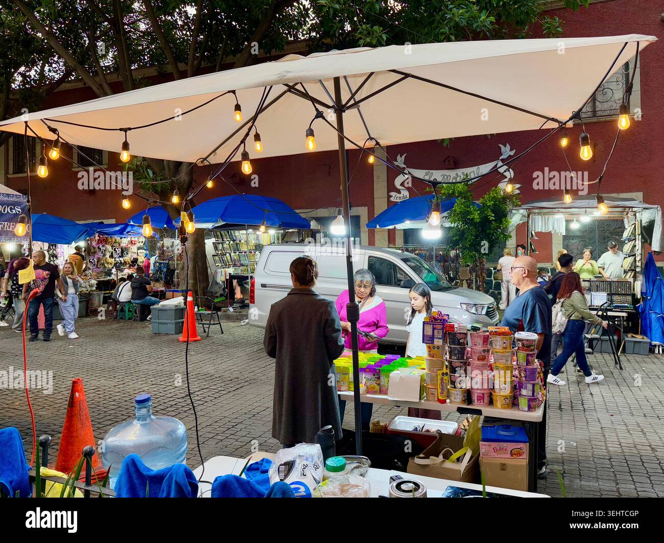 Gli amanti dello shopping serale curiosano tra le bancarelle che vendono spuntini, dolci e piccoli prodotti in un mercato di strada a Coyoacán, città del Messico, Messico Foto Stock