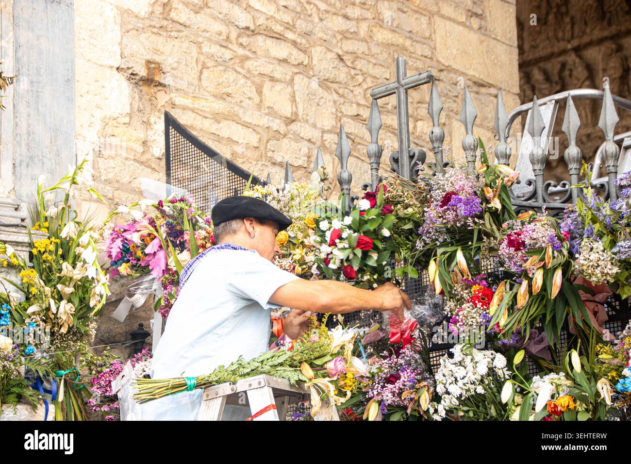 VITORIA-GASTEIZ, SPAGNA - AGOSTO 2025: Un uomo locale che indossa un tradizionale abbigliamento festivo con un berretto nero (txapela) si erge su una scala per organizzare il bouque Foto Stock