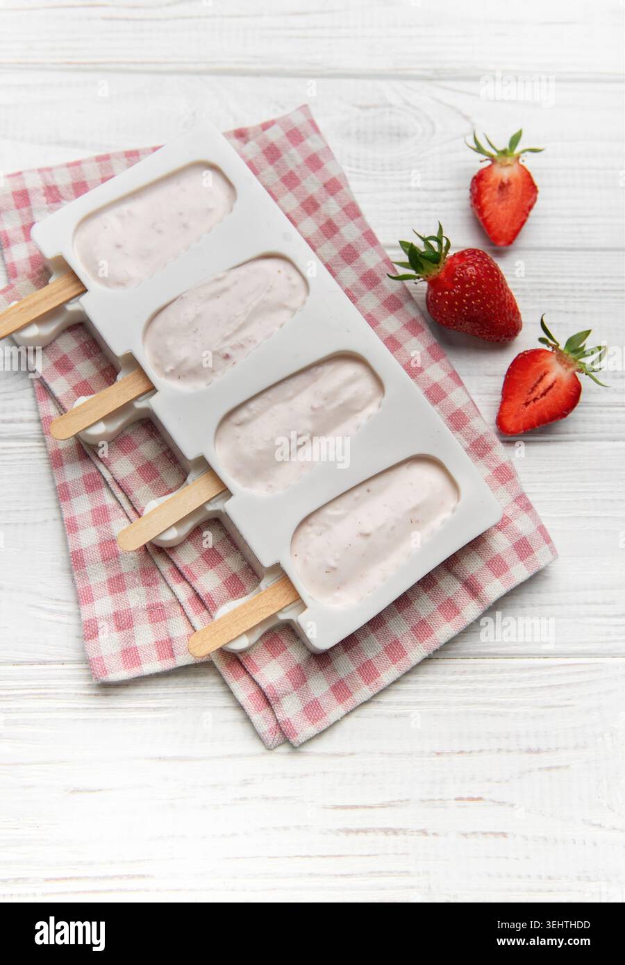 I papaveri di yogurt alla fragola vengono inseriti in una muffa su un tovagliolo a quadri con fragole fresche Foto Stock