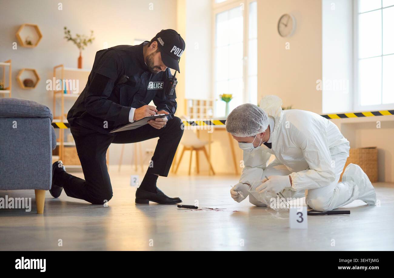 Un esperto forense di sesso maschile che raccoglie prove con l'agente di polizia durante le indagini per omicidio. Foto Stock