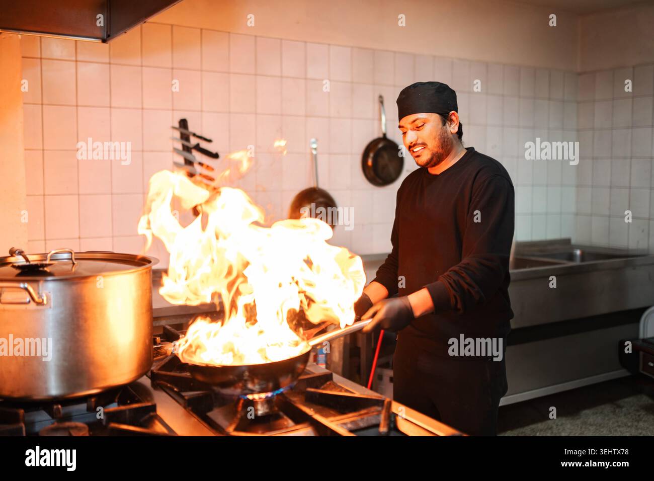 Lo chef maschile ha cucinato il cibo in una padella su una stufa Foto Stock