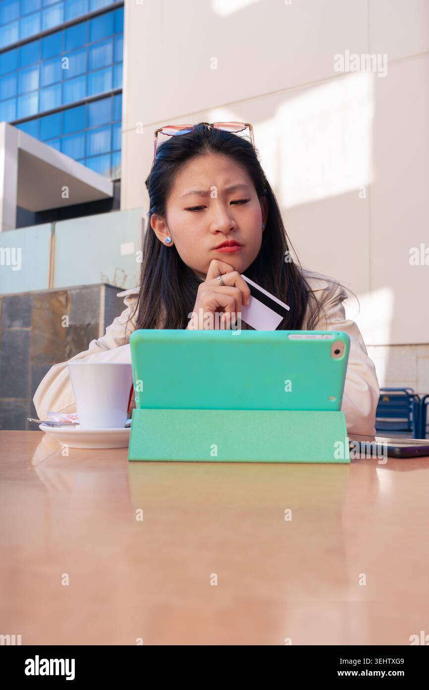 Persona concentrata che utilizza un tablet e una carta di credito per fare acquisti online sicuri all'aperto. Foto Stock