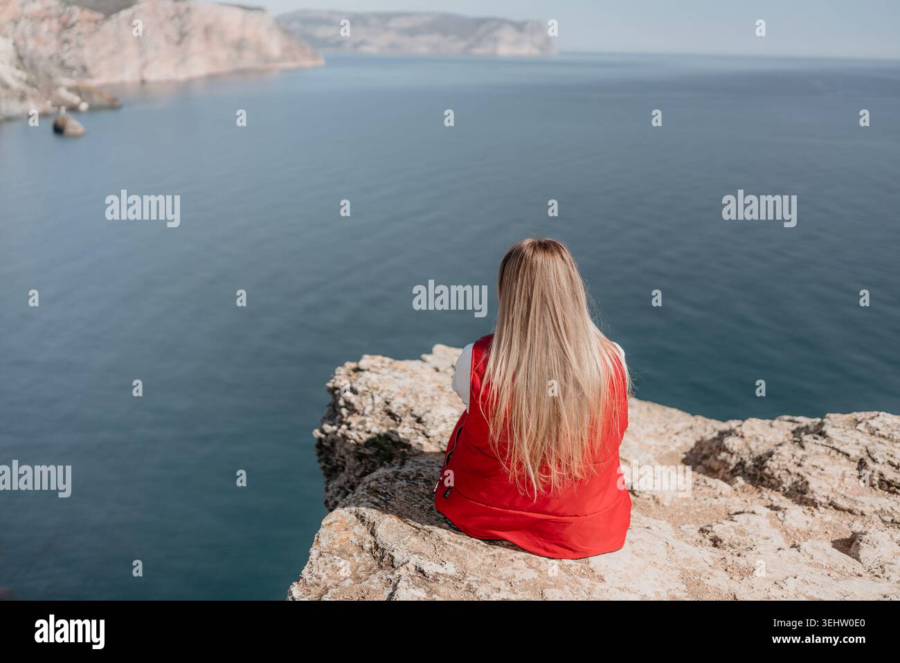 Donna sulla scogliera sul bordo di una montagna rocciosa che si affaccia sulle acque blu dell'oceano durante una giornata tranquilla Foto Stock