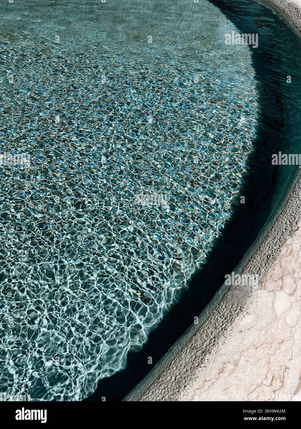 Acqua limpida della piscina con riflessi della luce del sole e bordi curvi, sfondo estivo astratto con increspature, ombre e texture rinfrescante Foto Stock