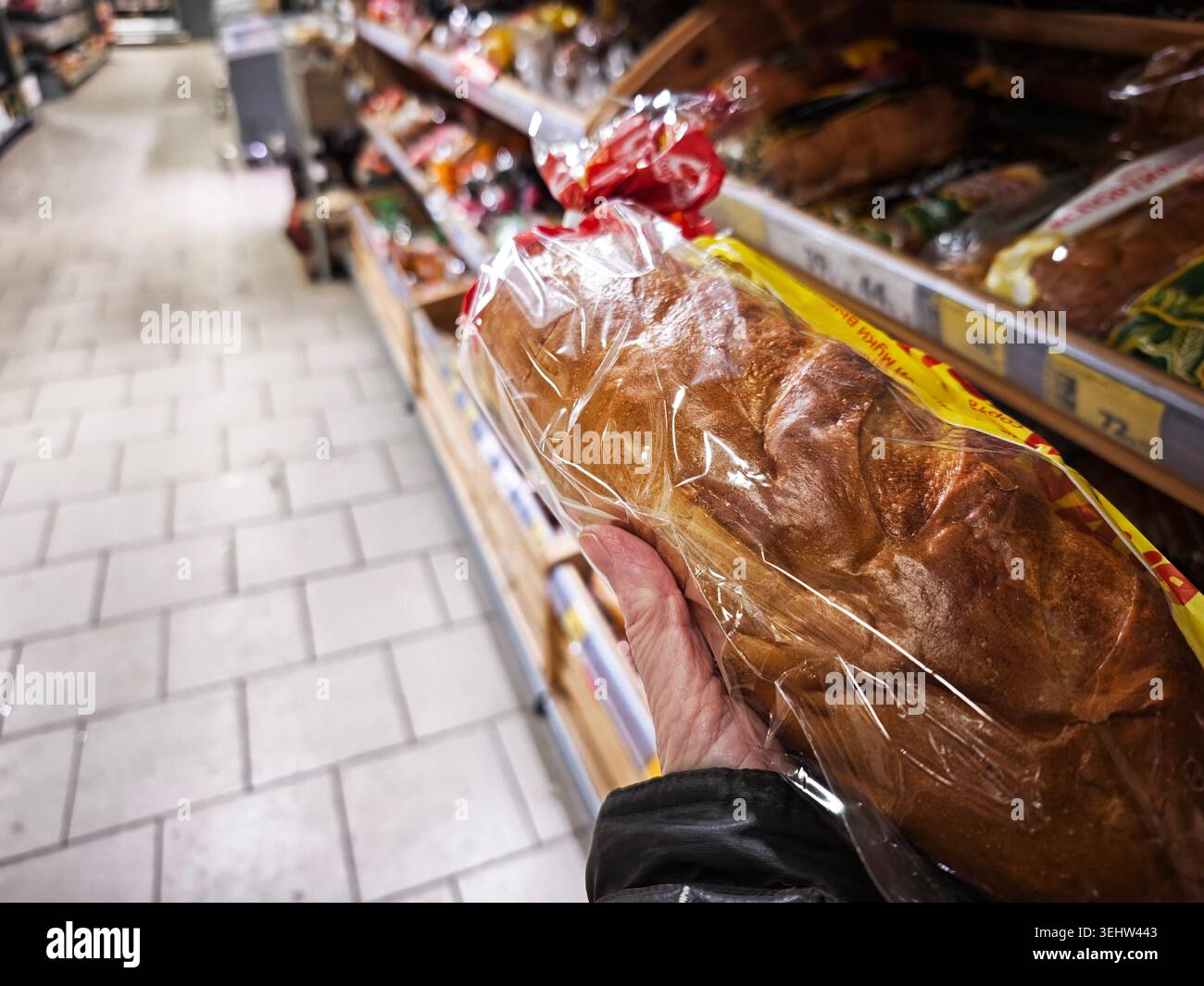 Un cliente preleva una pagnotta di pane da uno scaffale nel corridoio di un negozio durante un viaggio di shopping per acquistare articoli e generi alimentari giornalieri. Foto Stock