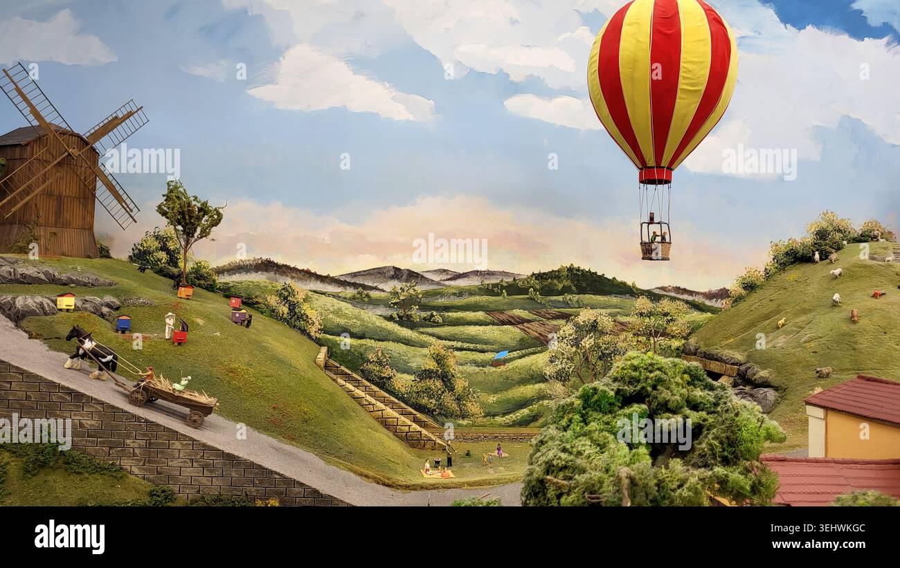 Mongolfiera che sorvola paesaggi in miniatura con mulini a vento e colline ondulate Foto Stock