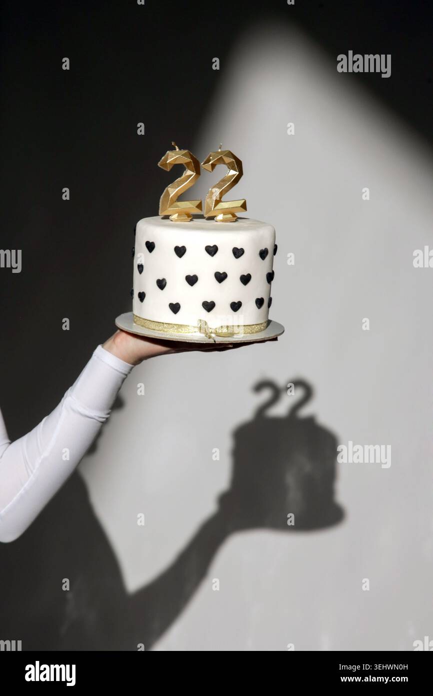 Primo piano di una torta di compleanno durante una ripresa in studio, torta bianca con cuori neri e candele dorate sotto una luce spettacolare Foto Stock