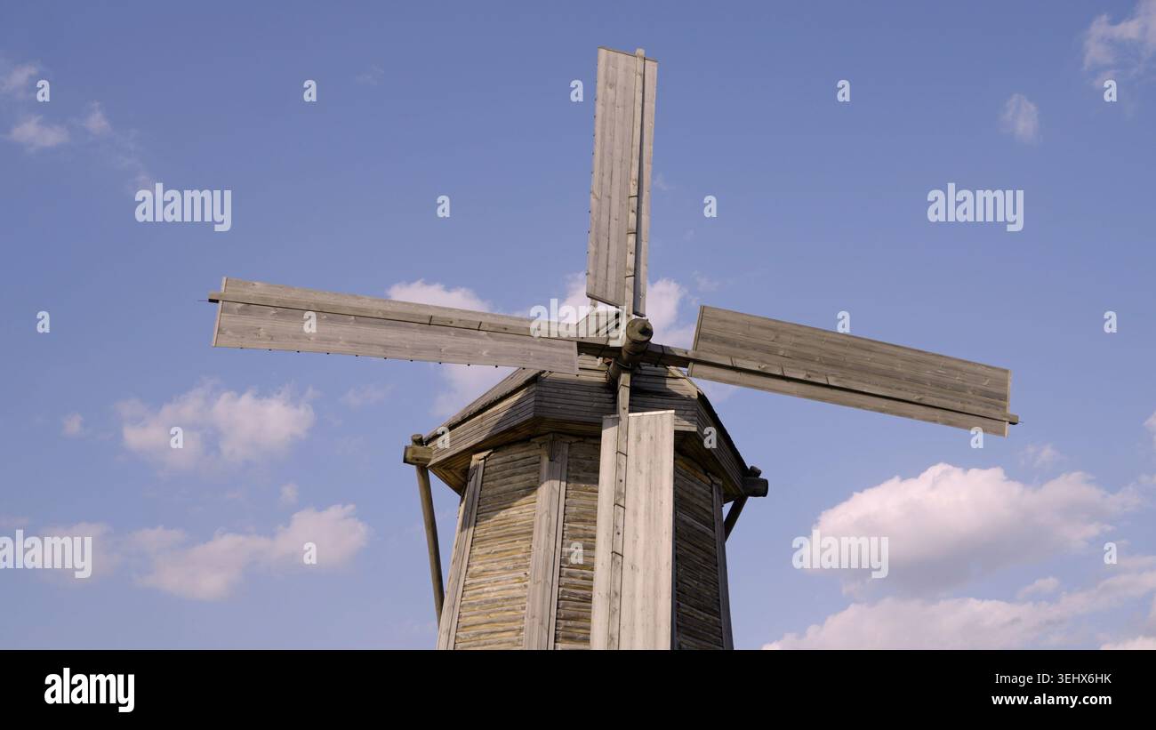 Colpo ad angolo basso di un mulino a vento in legno rustico con grandi vele contro il cielo blu. Giornata di sole e sole con nuvole bianche. L'illuminazione naturale crea tranquillità, nos Foto Stock