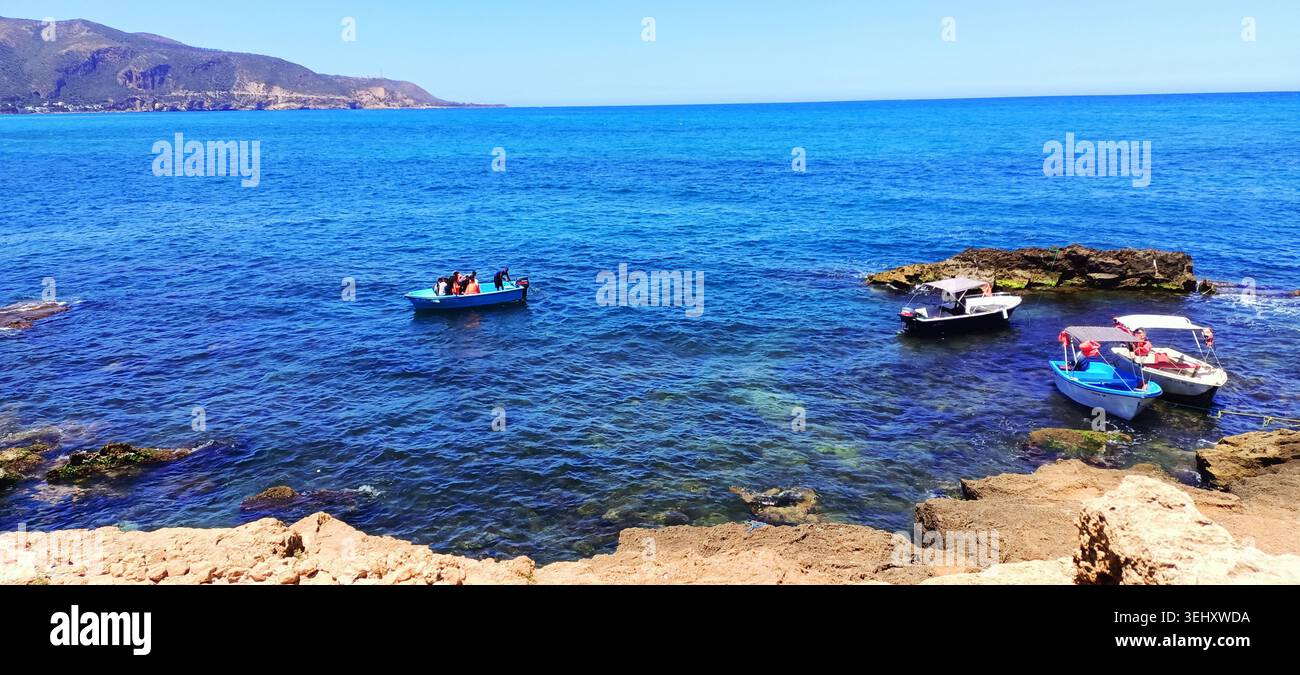 piccole imbarcazioni turistiche che galleggiano nel mare mediterraneo cristallino e turchese vicino alla costa rocciosa in una brillante giornata estiva. - Immagine stock catturata con smartphone