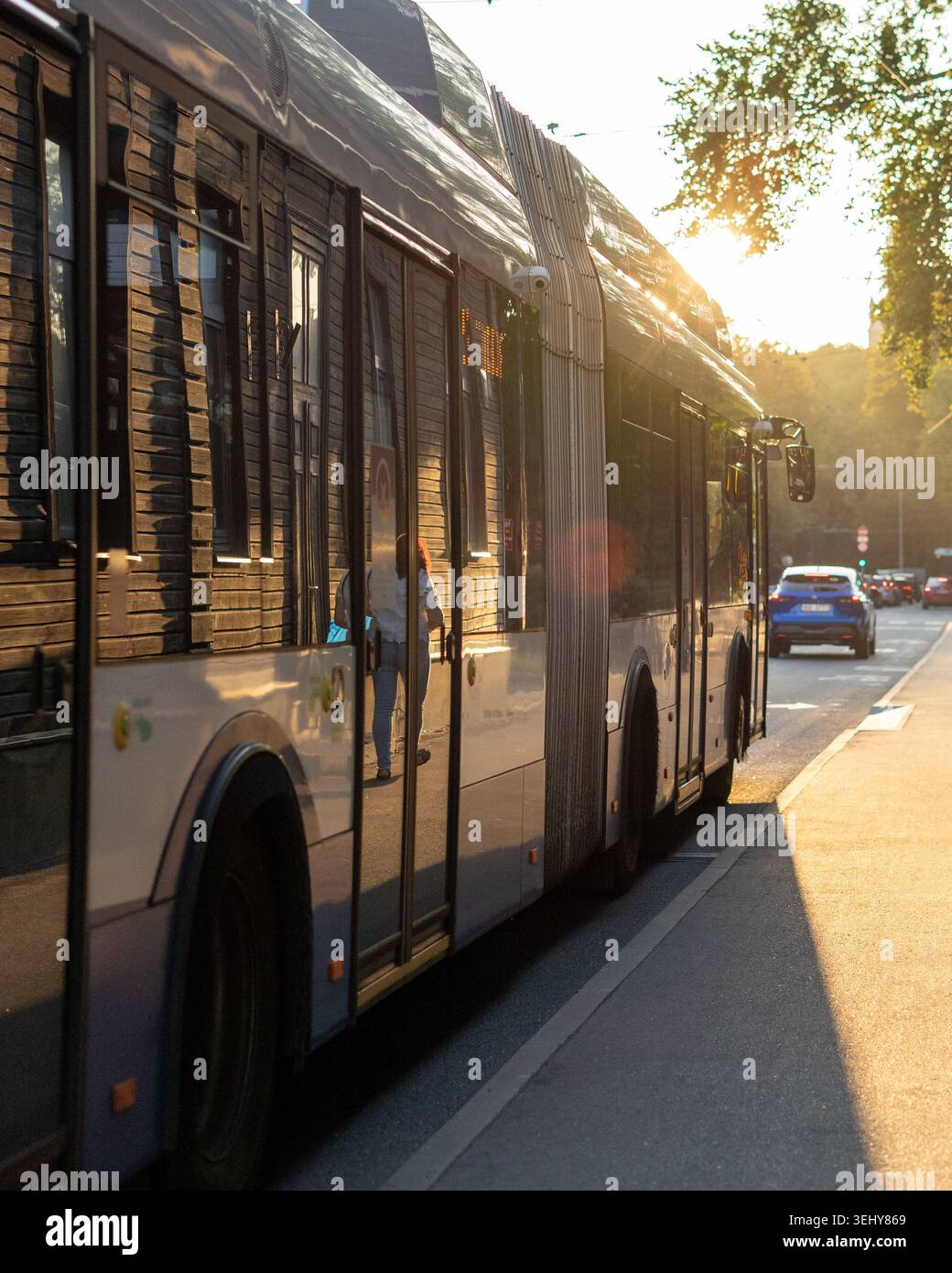 Un moderno autobus cittadino durante l'ora d'oro, con il sole basso che emette un caldo e radioso bagliore. Foto Stock