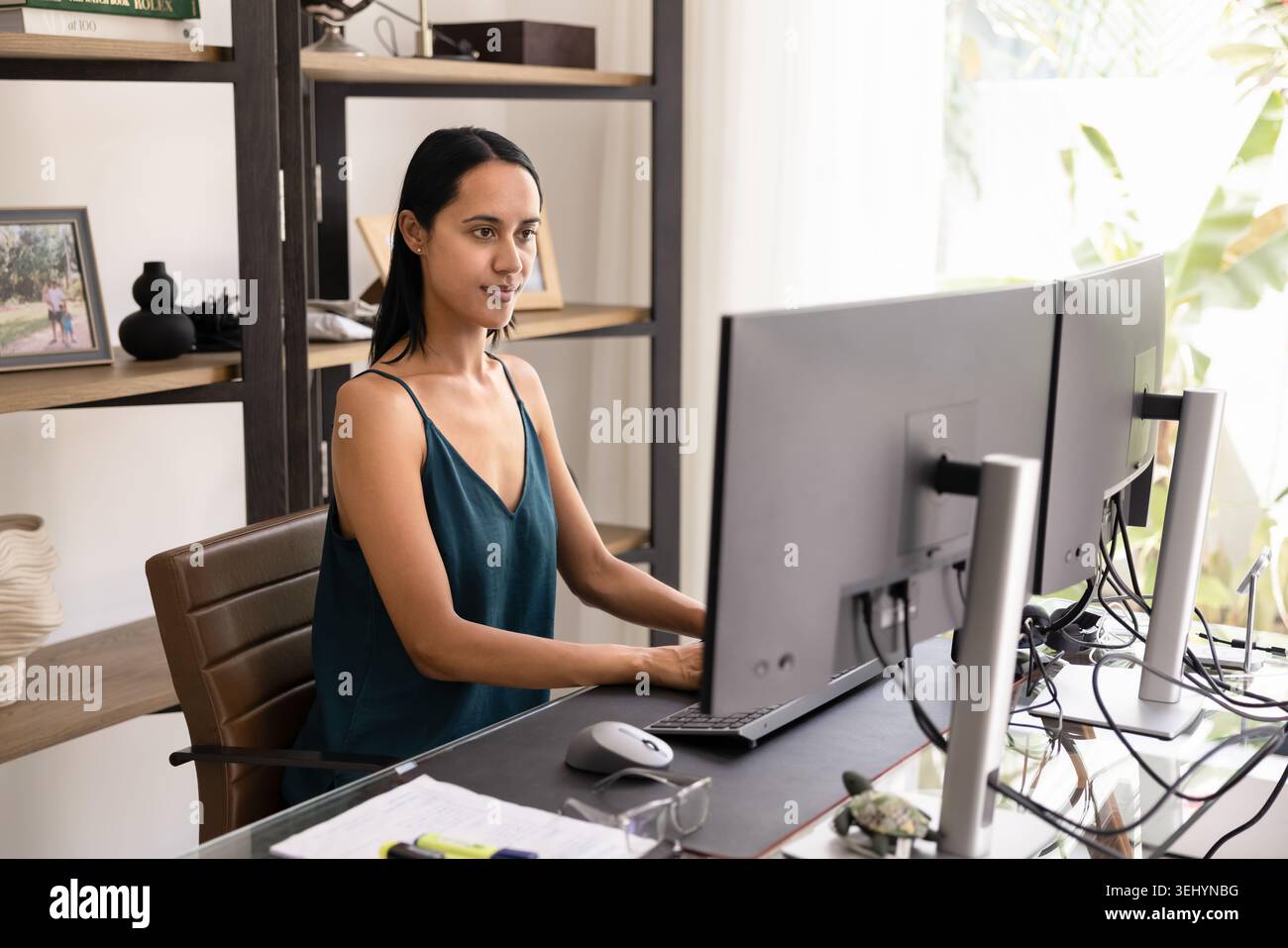 Donna concentrata che lavora su due monitor nell'ufficio domestico Foto Stock