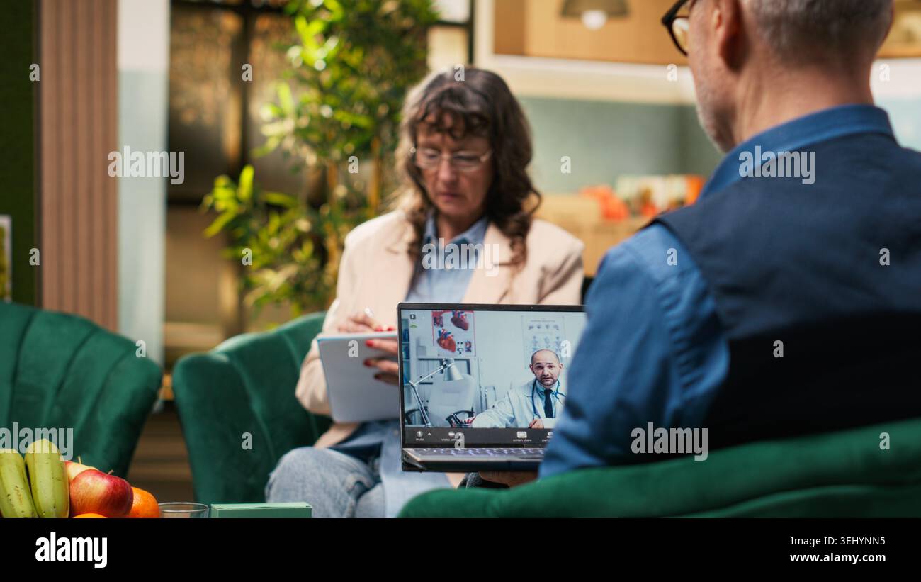 La pensionata prende appunti durante il controllo medico virtuale con il medico tramite videochiamata, ricevendo consigli sul trattamento e consigli professionali per il benessere e la vitalità. Lista di scrittura. Foto Stock