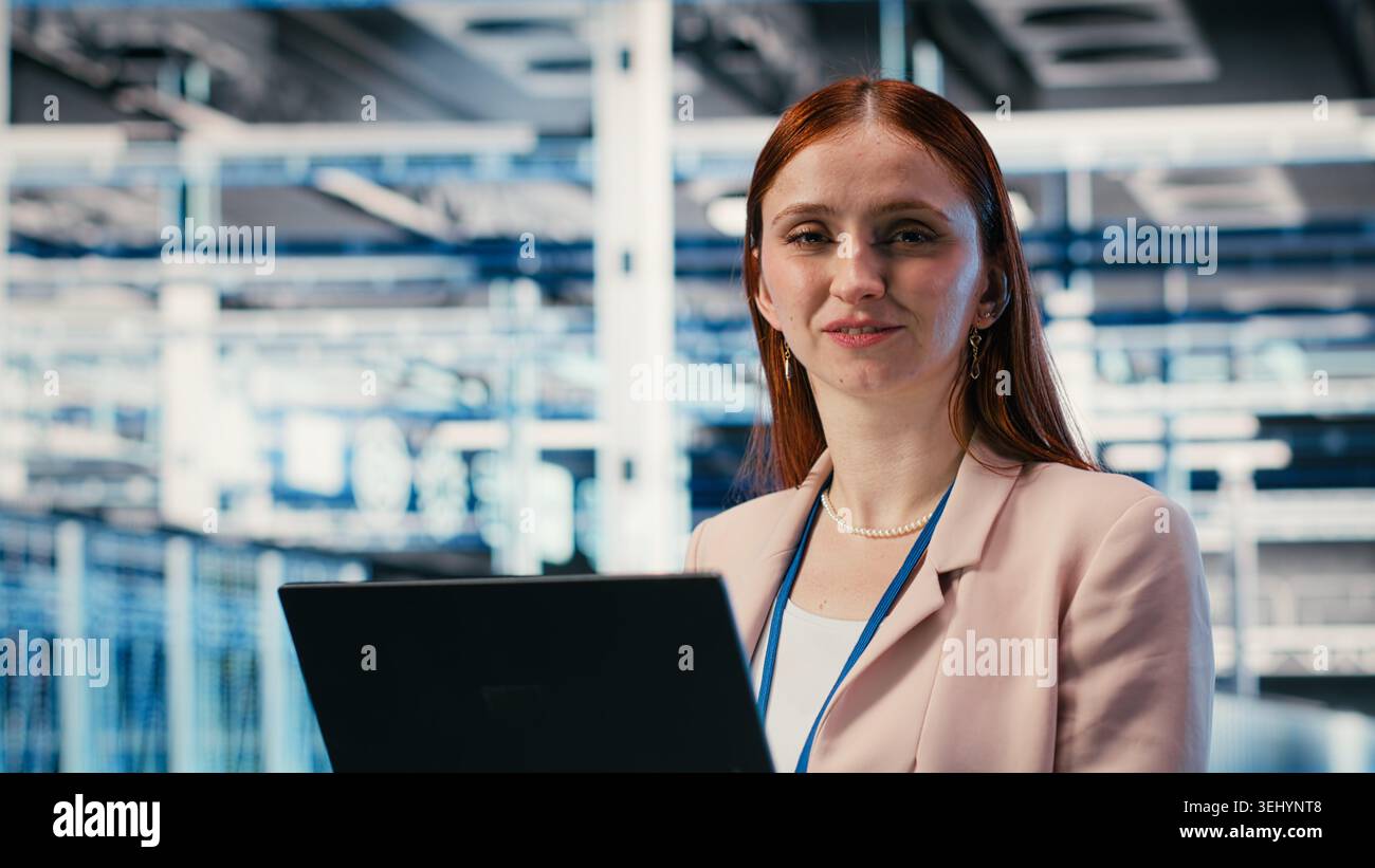 Donna felice in sala server che utilizza un notebook per migliorare l'efficacia operativa dell'infrastruttura. Gioiosa ingegnere donna nel data center che utilizza un notebook per monitorare le metriche di RIGS, telecamera B. Foto Stock