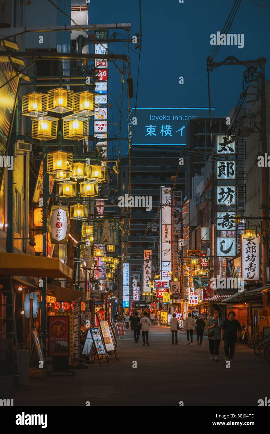Osaka, Giappone - 26 aprile 2026: Vista di una strada stretta di notte con lanterne luminose, insegne al neon e persone che camminano attraverso il quartiere di Dotonbori. Foto Stock