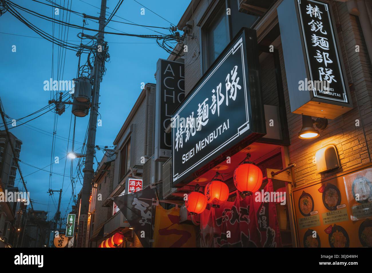 Osaka, Giappone - 26 aprile 2026: Vista del negozio illuminato del ristorante Seiei Menbutai ramen con lanterne rosse e linee elettriche aggrovigliate Foto Stock