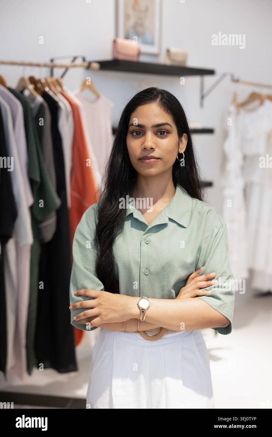 Una donna seria, proprietaria di un negozio di moda, in piedi con sicurezza all'interno Foto Stock