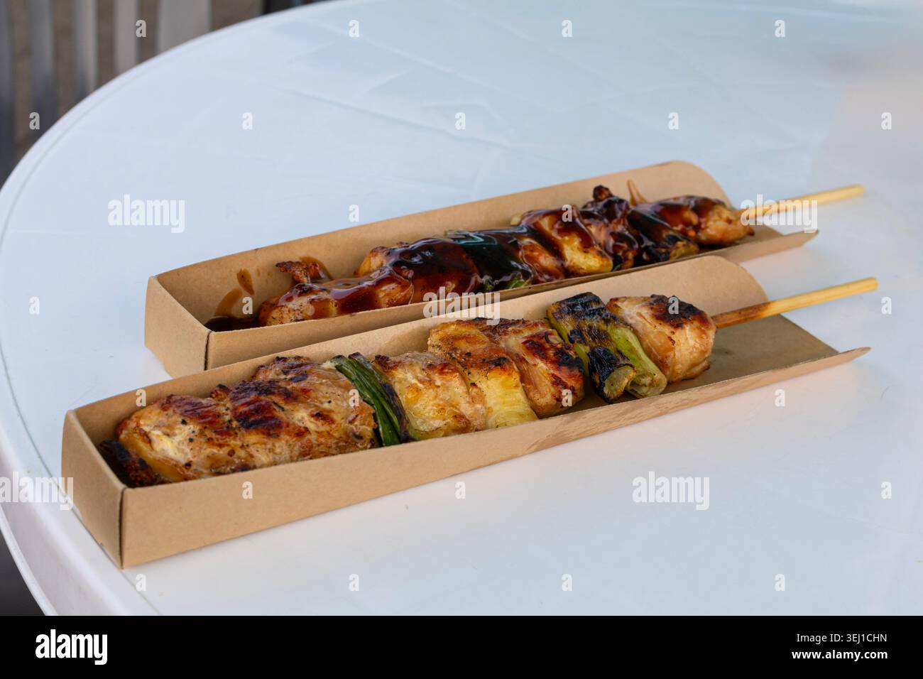 Primo piano di spiedini di pollo alla griglia con salsa glassata e verdure servite su un tavolo bianco all'aperto. Foto Stock