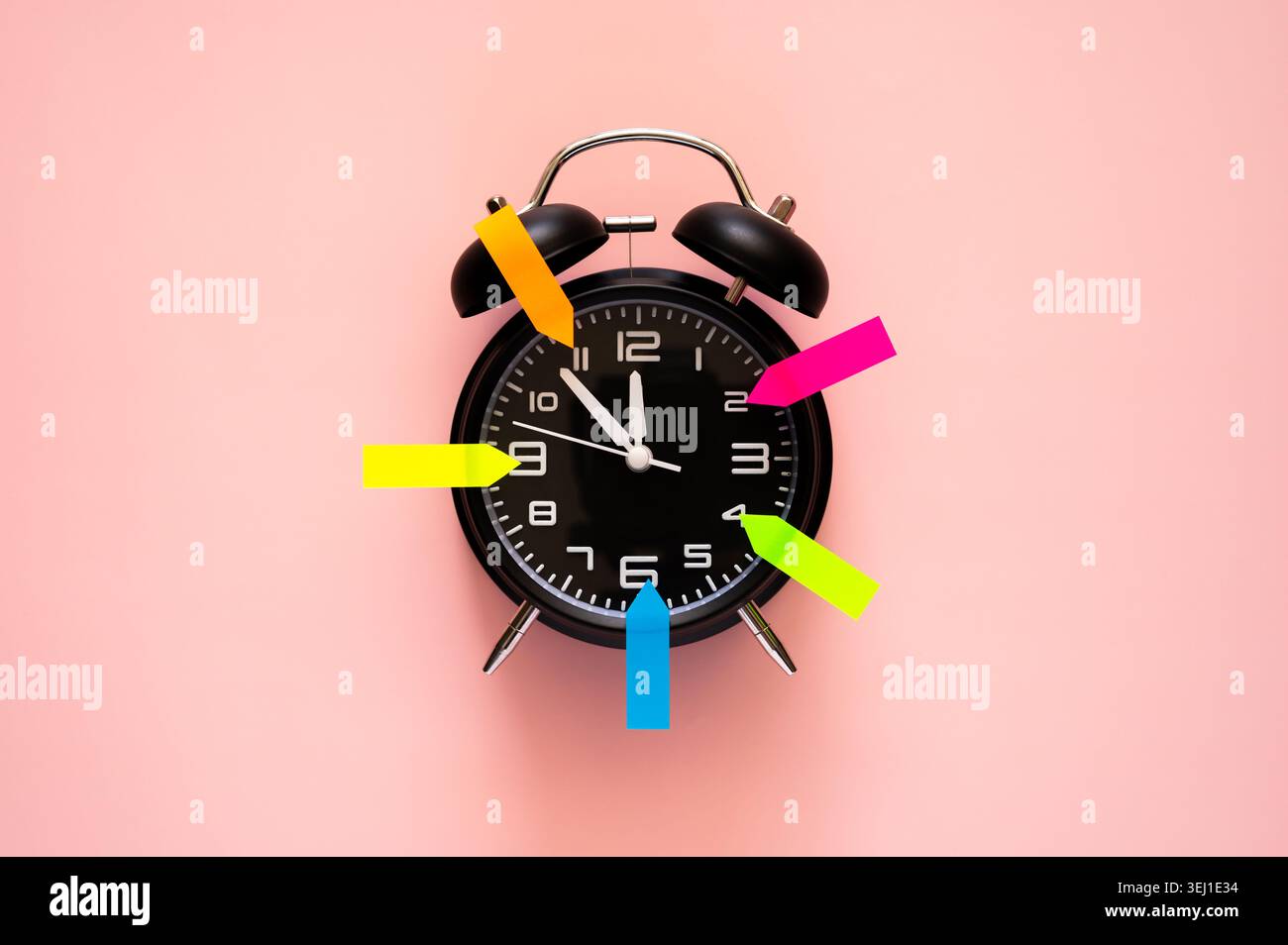 Una sveglia nera su uno sfondo rosa tenue con frecce colorate che segnano le ore. Foto Stock
