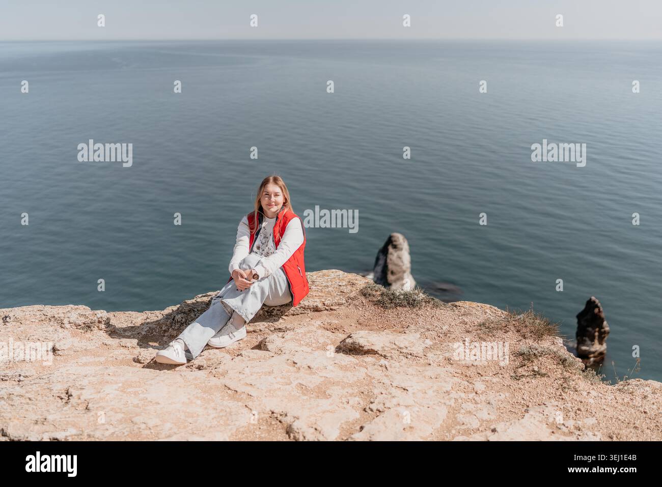 Donna sulla scogliera che siede sul bordo roccioso che si affaccia sul mare blu durante un viaggio avventura al sole con spazio per copiare Foto Stock