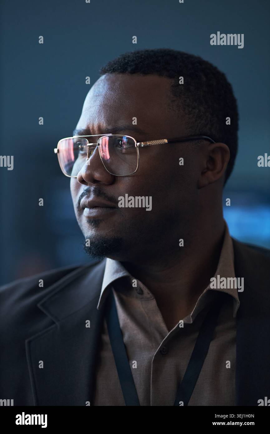 Immagine verticale di un uomo d'affari di mezza età nero che indossa occhiali da vista, con un'espressione mirata durante un evento aziendale. Adatto per leadership, strategia, branding esecutivo Foto Stock