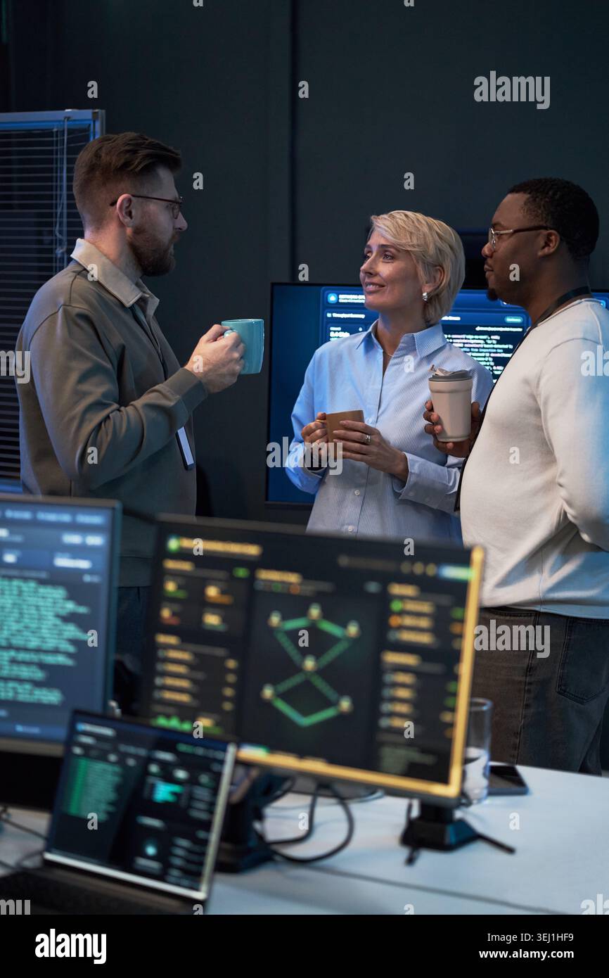 Ripresa verticale di diversi colleghi che discutono di progetti software durante una pausa caffè in ufficio tecnico. Concetto di collaborazione tra team e comunicazione sul luogo di lavoro per il marketing aziendale IT Foto Stock