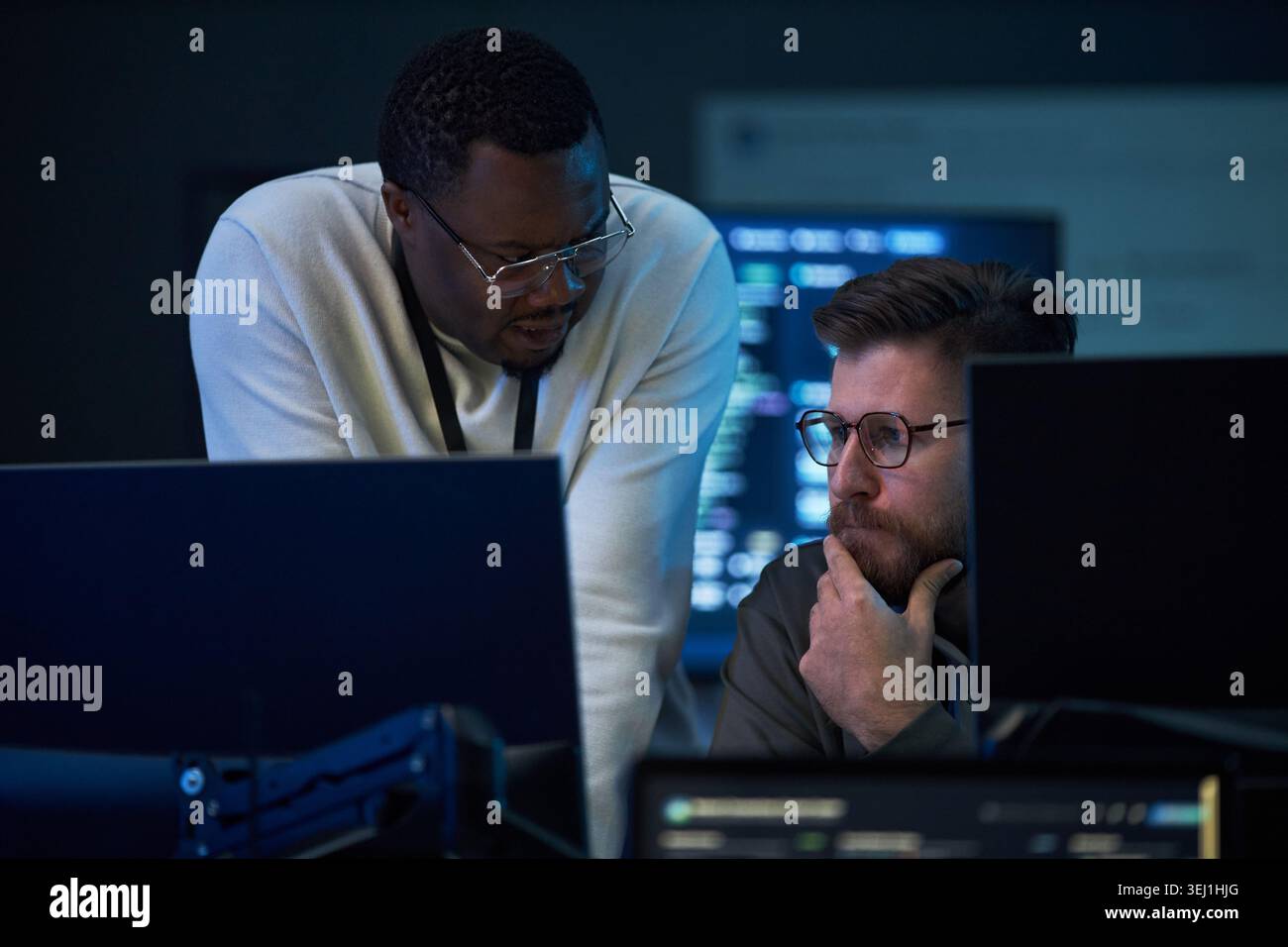 Uomo afroamericano e caucasico che rivedono il codice su monitor desktop, collaborando alla risoluzione dei problemi nell'ufficio IT. Ideale per sicurezza informatica, sviluppo software, marketing di squadra Foto Stock